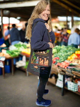 Woman holding a colorful tote bag with a design at an outdoor market.