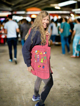 Person holding a large pink backpack with colorful designs outdoors.
