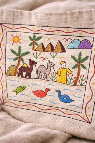 Embroidered scene on fabric with palm trees, pyramids, and people.