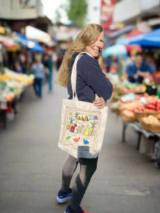 Woman carrying a tote bag with colorful designs at an outdoor market.