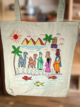 Tote bag with colorful hand-painted design of pyramids, camels, and people on a wooden surface.