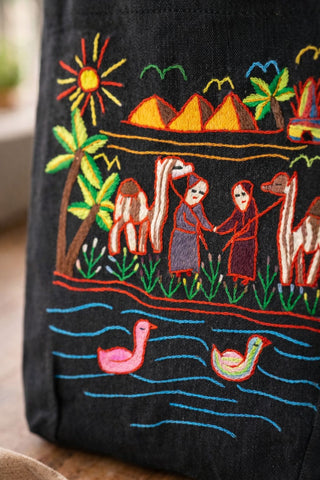 Embroidered scene on a black fabric with colorful designs of people, animals, and nature.