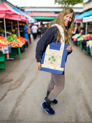 Person holding a blue and white tote bag with a design, standing on a boat.