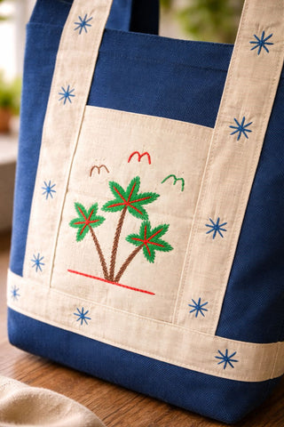Blue tote bag with embroidered palm tree design on a wooden surface