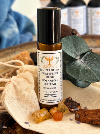 Egyptian Botanicals Juniper Berry Grapefruit Musk Botanical Perfume in a 10ml rollerball bottle, styled with natural ingredients, a drawstring bag, and a eucalyptus leaf.