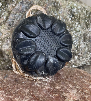 Charcoal and Loofah Foot Scrub Soap Bar leaning against a rock with twine string