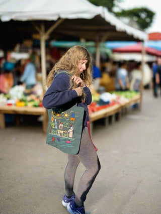 Person holding a colorful tote bag in front of a building with large windows.