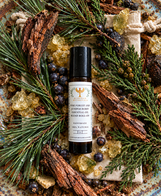 A bottleof a natural botanical perfume roll on Pine Forest-Natural Botanical Perfume by Egyptian Botanicals  styled in a flat-lay arrangement with pine needles, juniper berries, crystals, and wood bark on a rustic ceramic plate..