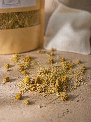 Dried herbs on a sandy surface with a paper bag in the background