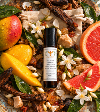 A bottle of handcrafte natural botanical perfume roll on Egyptian Mango and Grapefruit Natural Botanical Perfume by Egyptian Botanicals surrounded by fresh ingredients including mango,and white jasmine flowers on a rustic stone surface.
