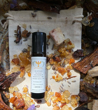A bottle of Egyptian Mango and Grapefruit Natural Botanical Perfume placed on a canvas drawstring bag, surrounded by crystals, dried flowers, and wood pieces.