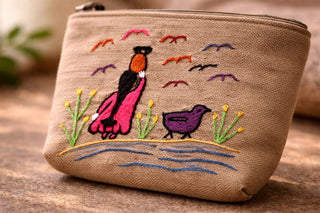 Beige pouch with embroidered design of a woman and birds on a wooden surface