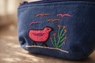 Blue pouch with pink embroidered bird and green plants on a wooden surface