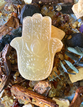 A carved Hamsa hand Egyptian Musk Hamsa Soap Bar –Natural Botanical Moisturizing Soap displayed on a bed of dried botanicals, bark, and small crystals.