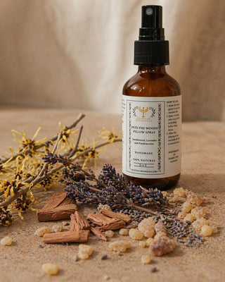 A bottle of natural pillow spray with a label, surrounded by dried lavender and herbs on a wooden surface.