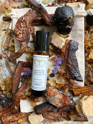 A bottle of Jasmine Rose Natural Botanical Perfume Roll-On  is displayed on a canvas stand, surrounded by natural ingredients, crystals, and wood pieces.