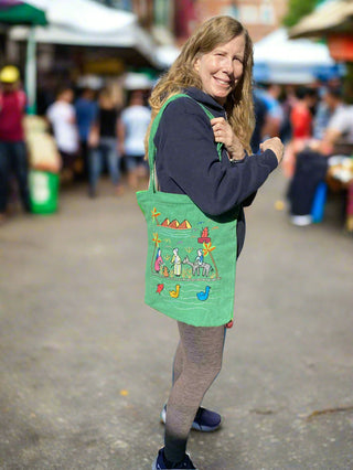 Woman holding a green tote bag with colorful designs at an outdoor market.