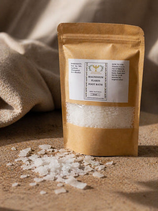 Brown paper bag of magnesium flakes foot bath with scattered flakes on a beige surface