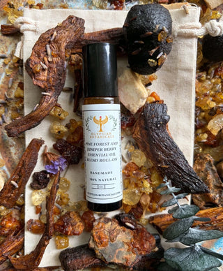 A roll-on essential oil bottle labeled 'Egyptian Botanicals Pine Forest and Juniper Berry Essential Oil Blend Roll-On' placed on a beige fabric pouch, surrounded by dried herbs, crystals, and botanical elements.