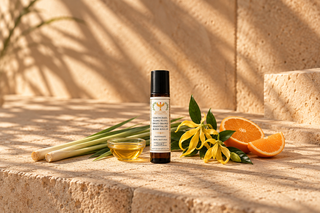 A 10 ml amber roll-on bottle of Lemongrass, Ylang Ylang & Sweet Orange Natural Botanical Perfume surrounded by natural ingredients Lemongrass, Ylang Ylang & Sweet Orange and jojoba oil on a sandy surface.
