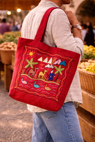 Person holding a red embroidered tote bag at an outdoor market.