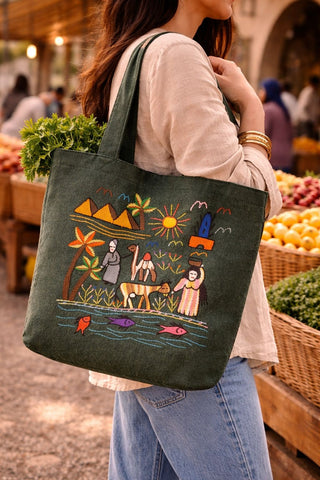 Person holding a green tote bag with colorful designs in an outdoor market setting